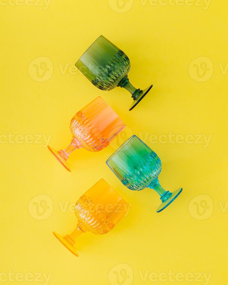 Colorful cocktail drinking glasses on bright yellow background. Minimal drink concept. Trendy summer party idea. Flat lay style. Top view. photo