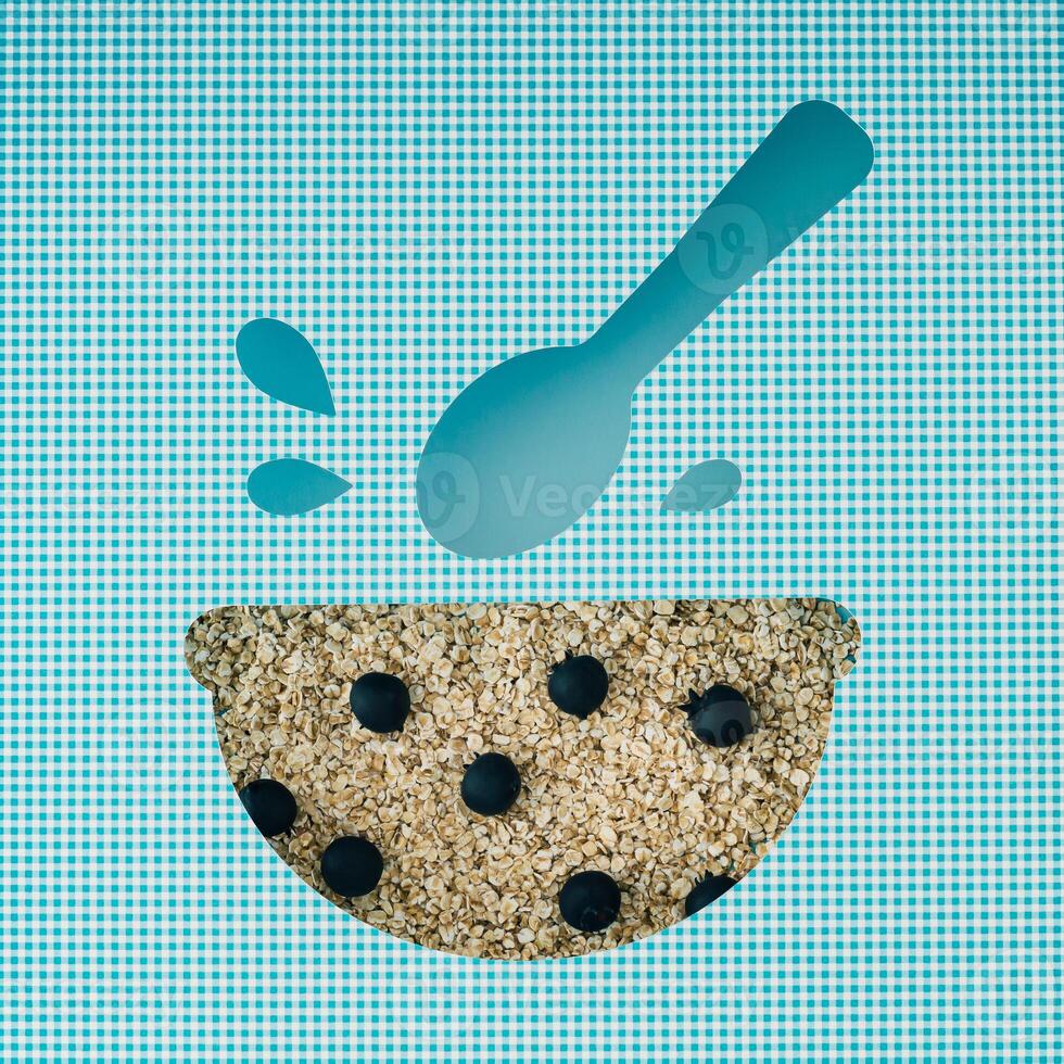 Oat flakes and fresh berries visible through a bowl and spoon shaped cutout on white and blue background. Conceptual food backdrop of musli and granola. Creative healthy breakfast flat lay. Top view. photo