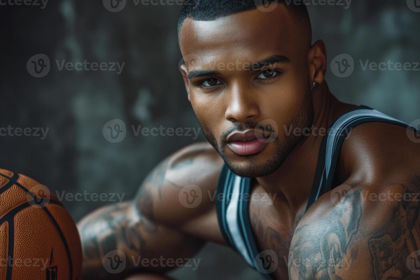 Handsome basketball player with athletic build holds ball, showcasing tattooed arms and low haircut against textured backdrop photo
