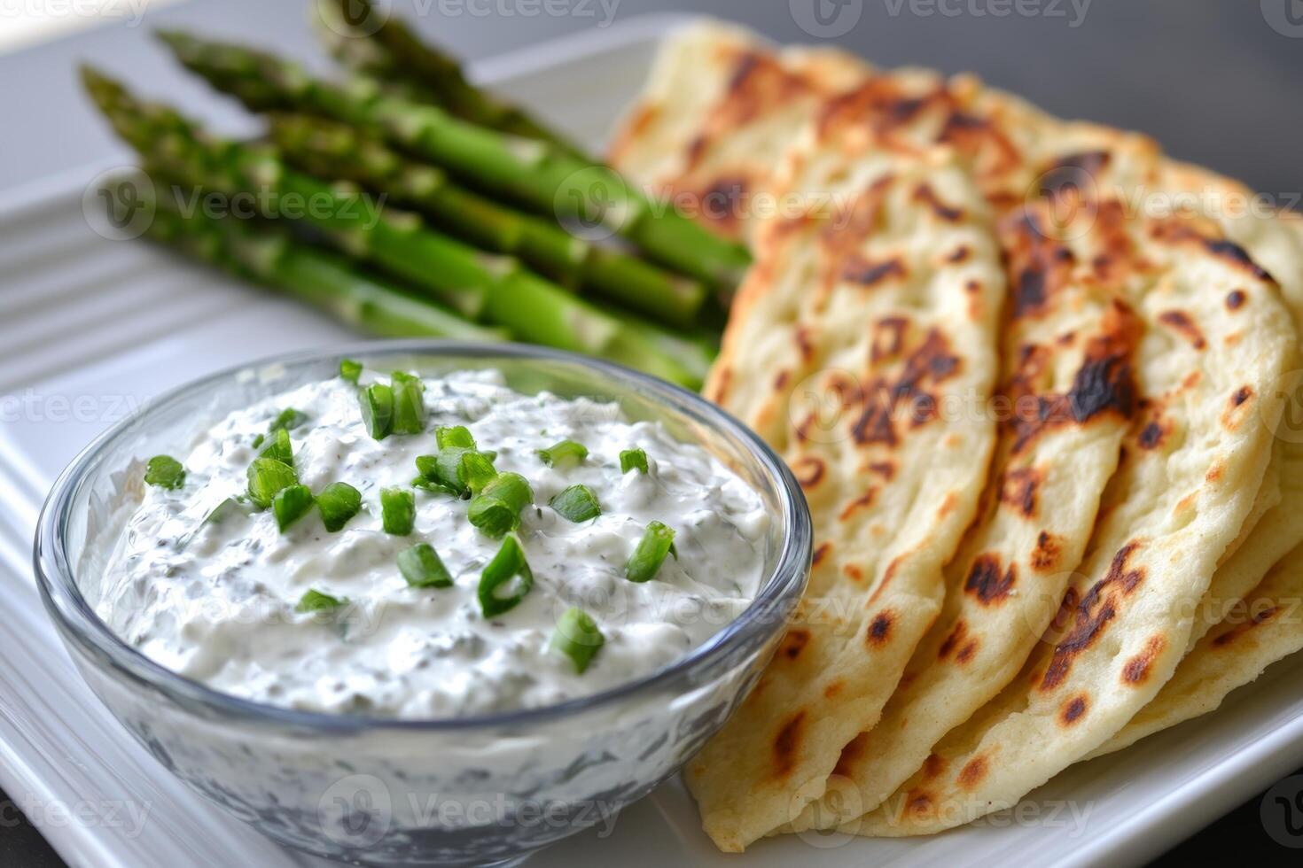 Delicious grilled asparagus served with creamy tzatziki and warm flatbreads on a plate in a casual dining setting photo