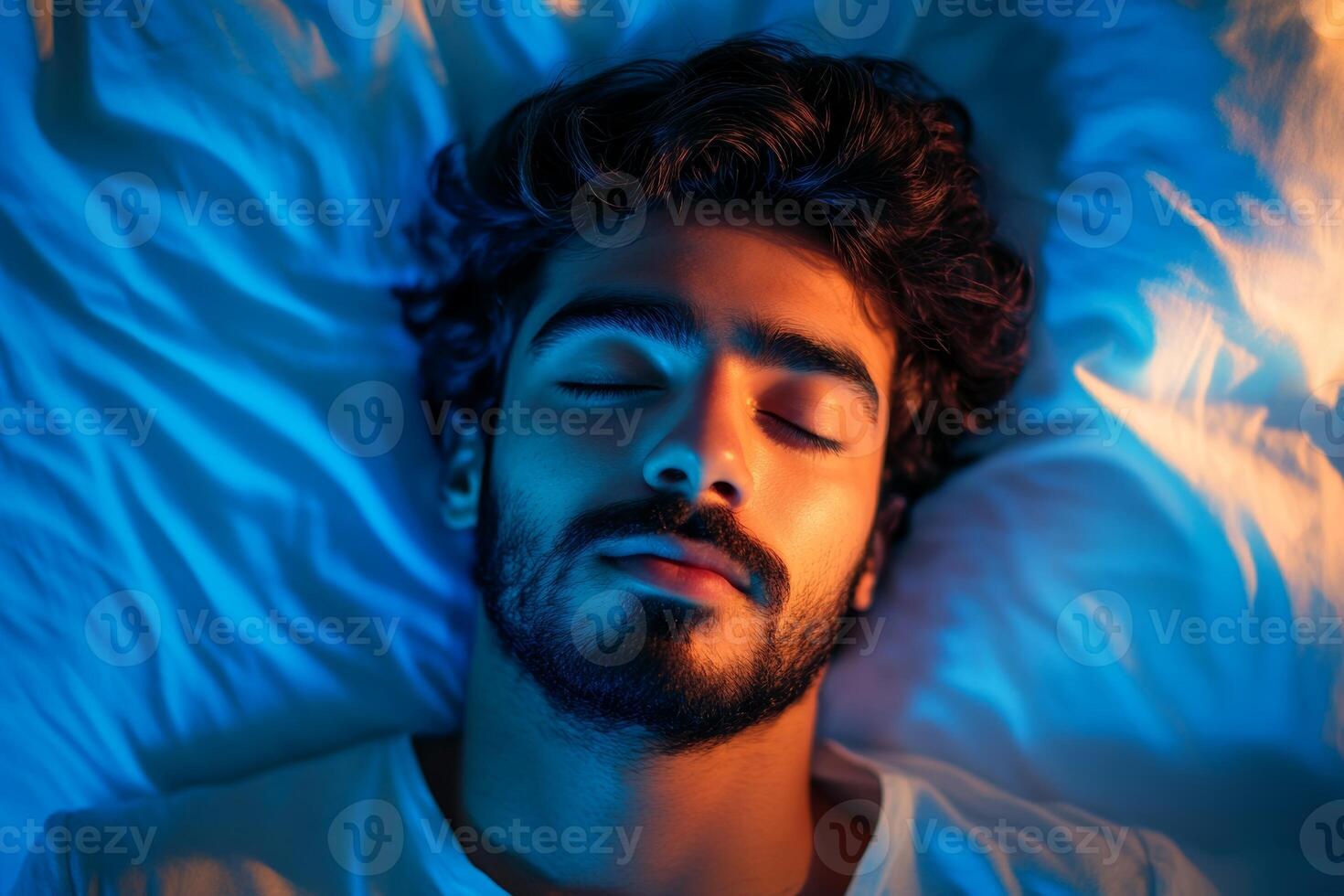 Young Arabic man peacefully sleeping in a cozy bedroom at night with soft blue light illuminating the space photo