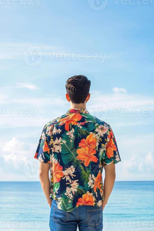 Man in floral shirt enjoys a serene beach view with clear blue skies and calm waves in the background during summer photo