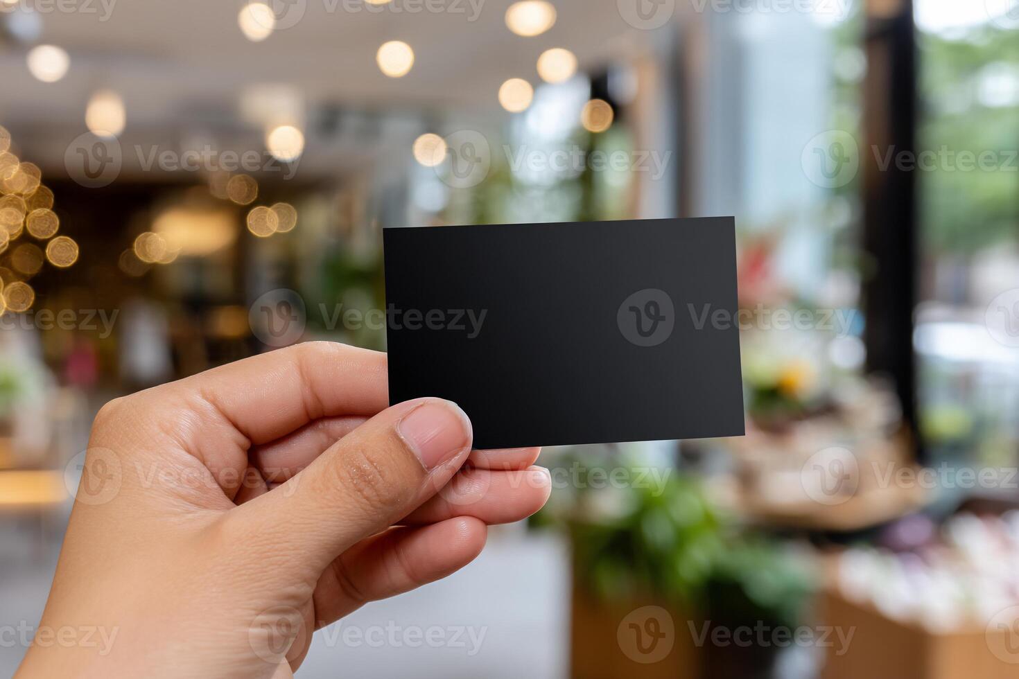 Hand holding a blank black business card in a modern, blurred interior setting photo