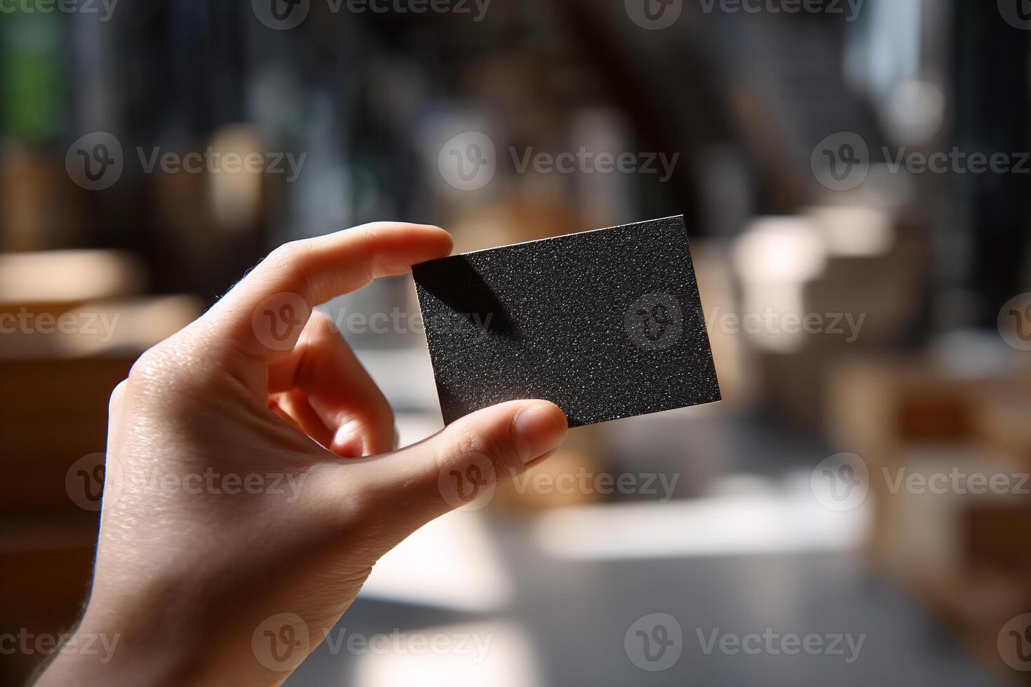 A hand holds a dark gray square piece of material. Blurred industrial background photo