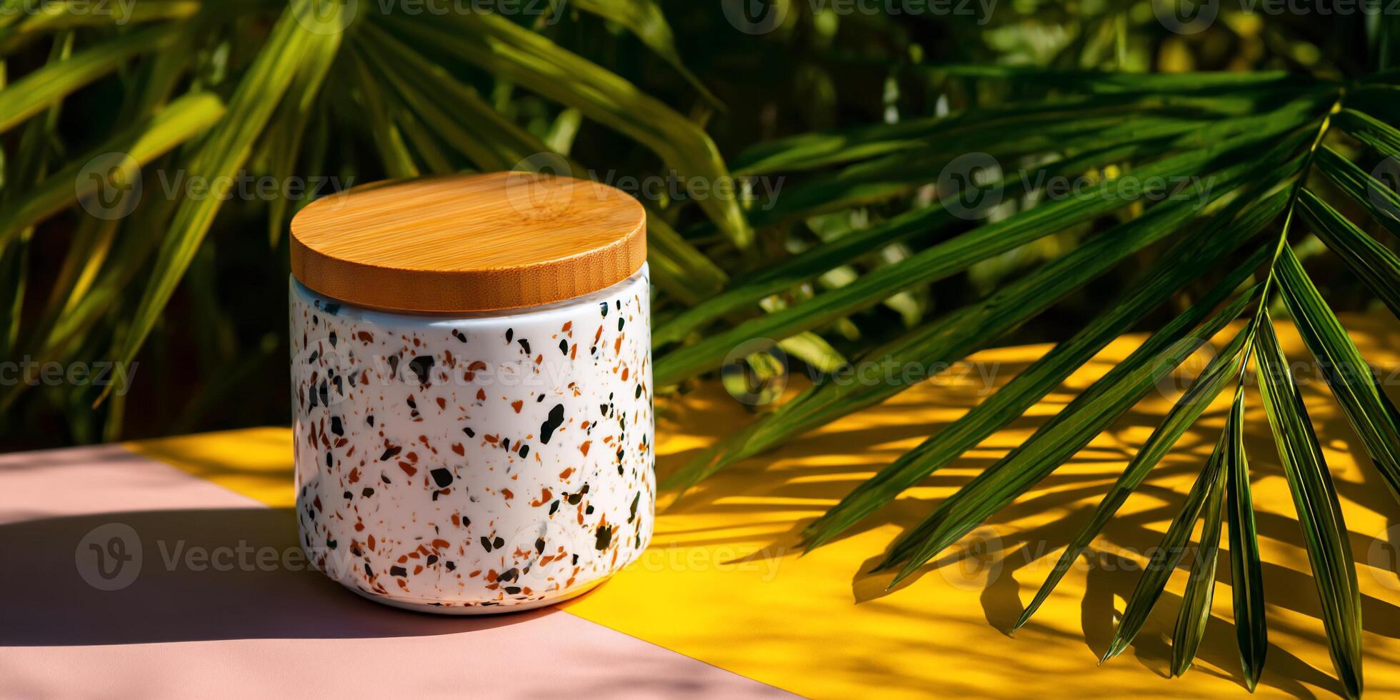 Terracotta-colored speckled ceramic container with a natural wooden lid, set on a yellow and pink surface, surrounded by palm fronds photo