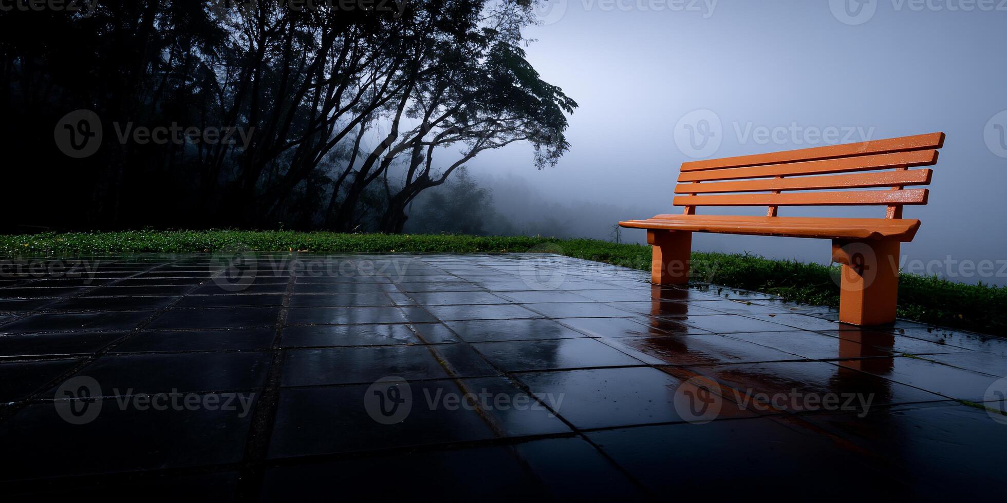 Empty orange wooden park bench on a wet paved path, misty trees in the background photo