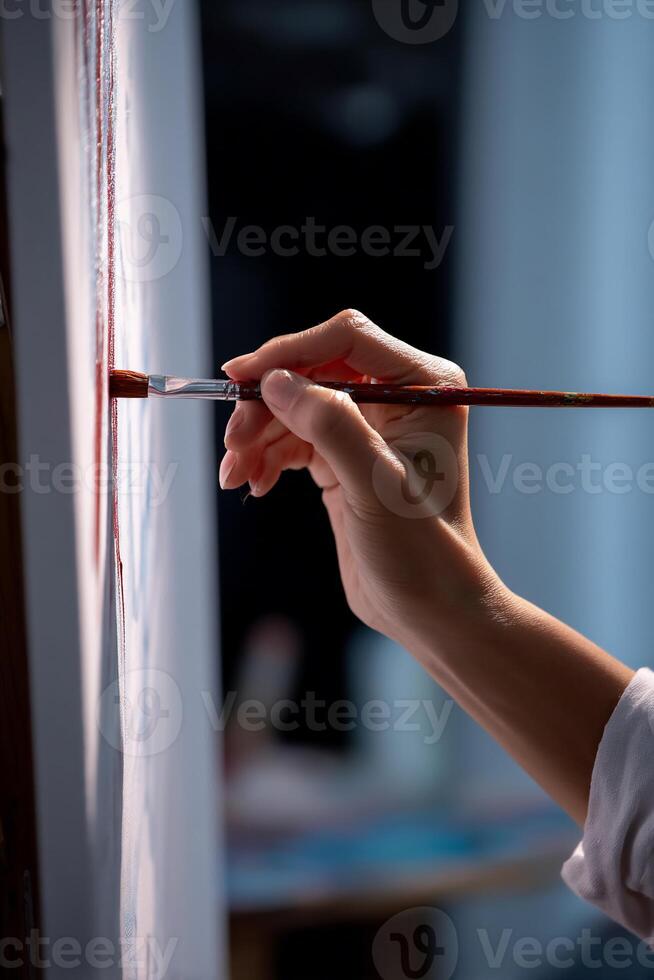 A person is holding a paintbrush and painting on a white canvas photo