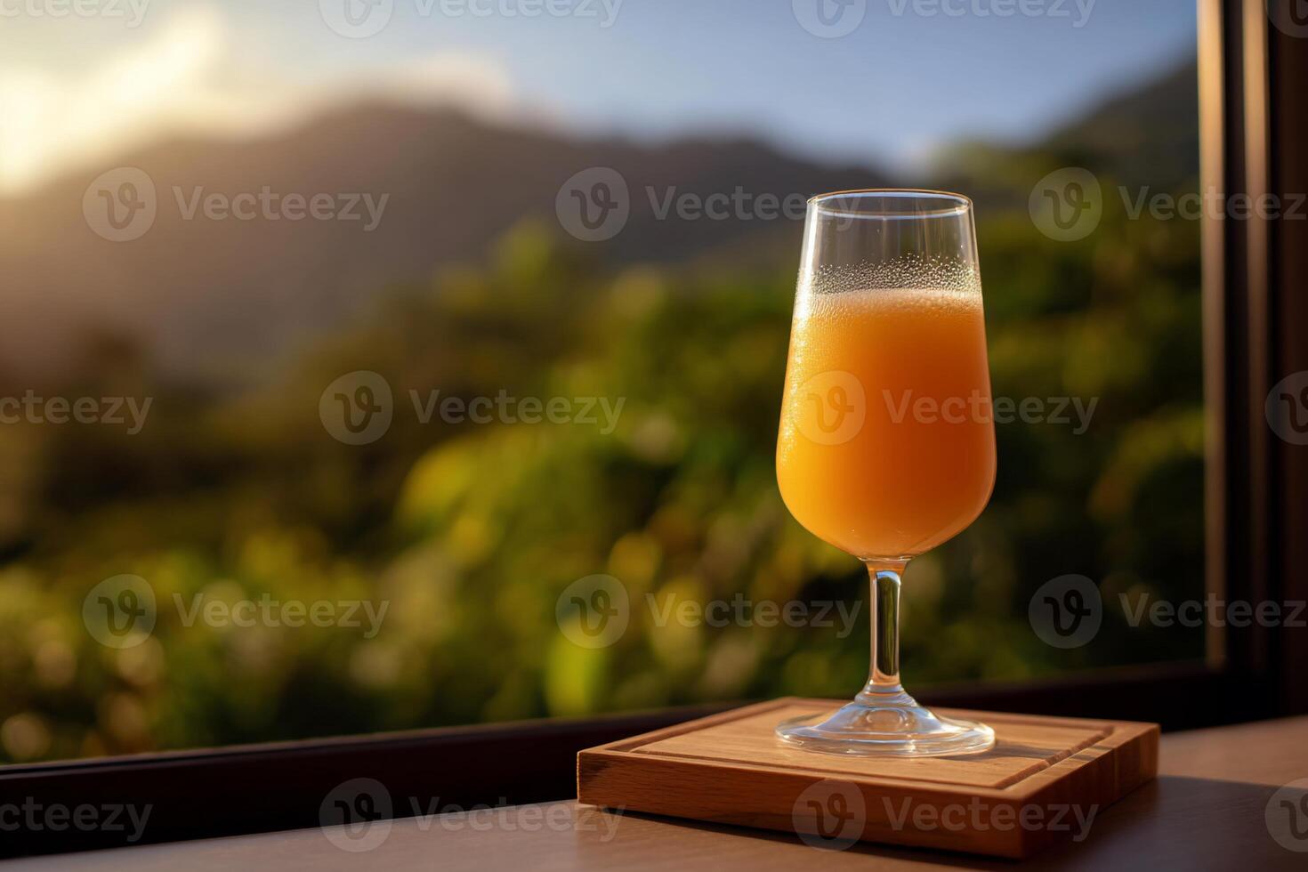 Sunset cocktail, a pale orange drink in a stemmed glass on a wooden coaster by a window overlooking a landscape photo
