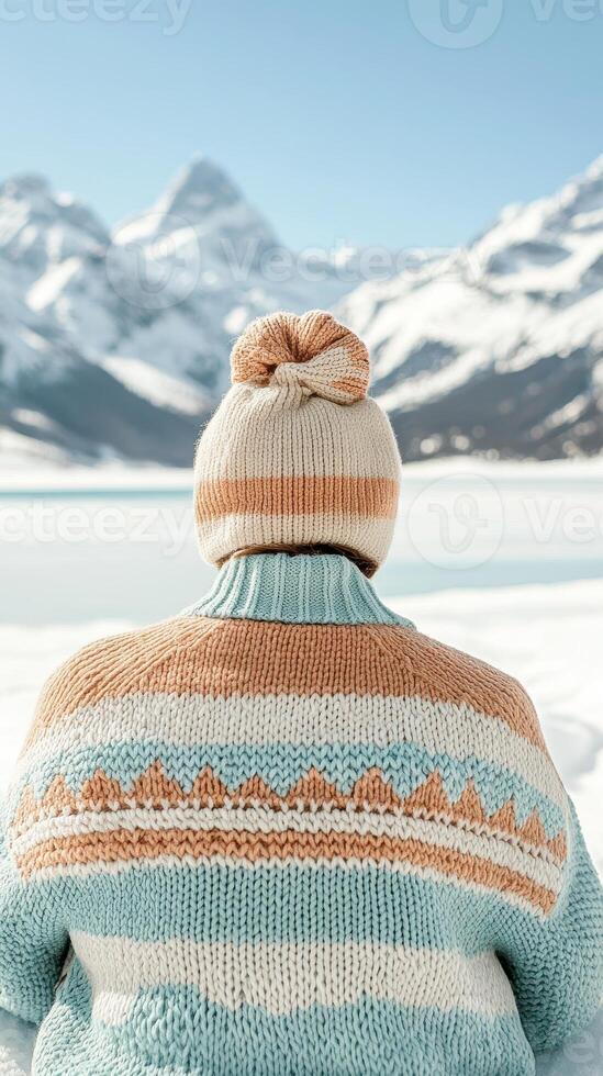 Knitted hat and sweater, person looks at snow covered mountains and icy lake. Bright sunny day in alpine environment. Winter scene. photo