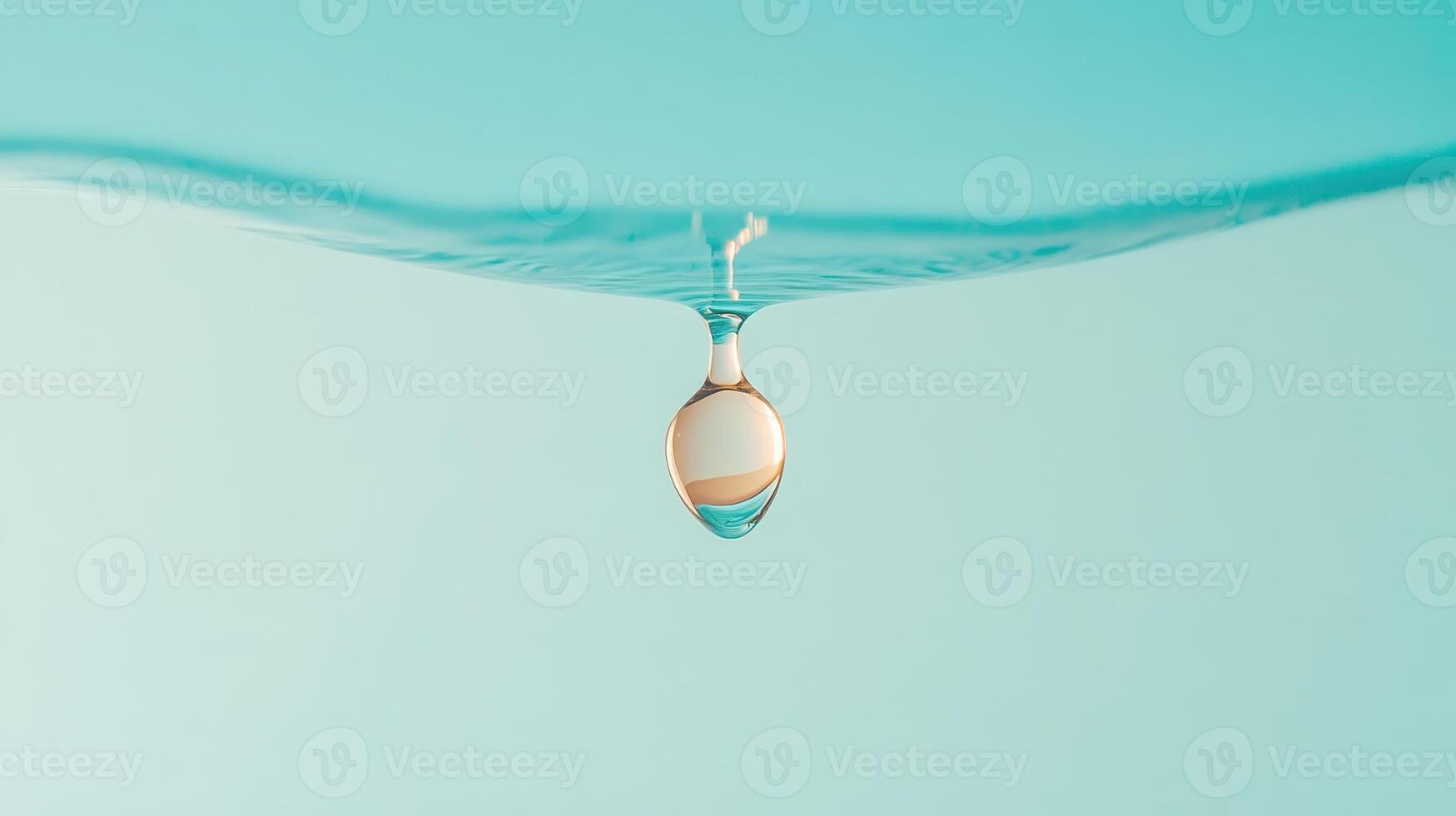 Liquid drop hangs beneath smooth water surface against a soft teal background. Clarity and light reflect in sphere shape. Close view. photo