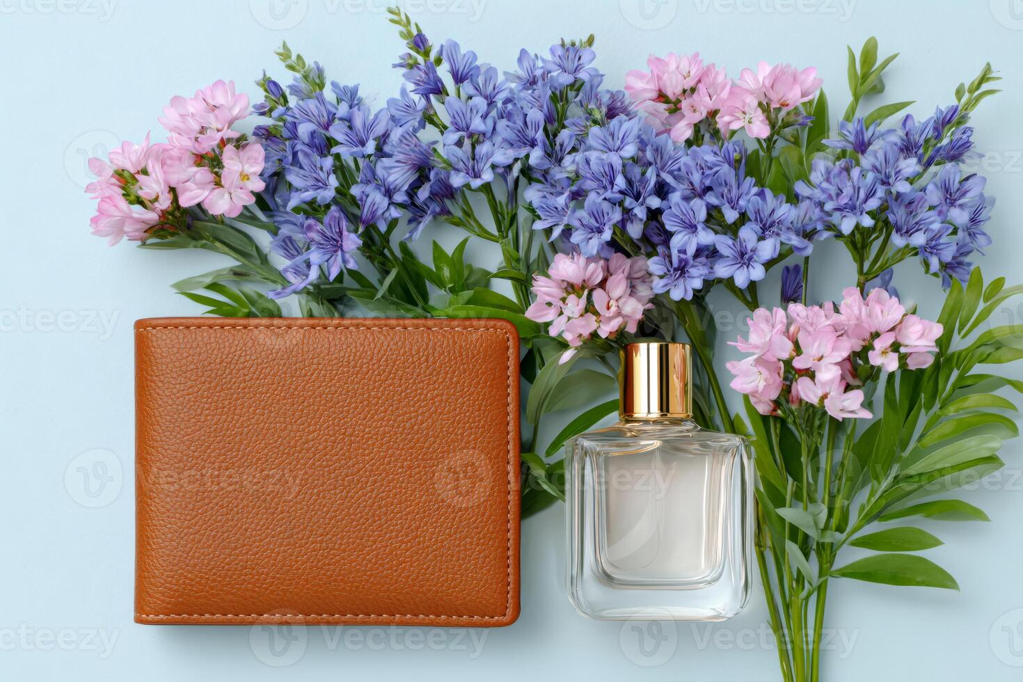 Brown leather wallet and perfume bottle lying near bouquet of pink and blue flowers on light blue background photo