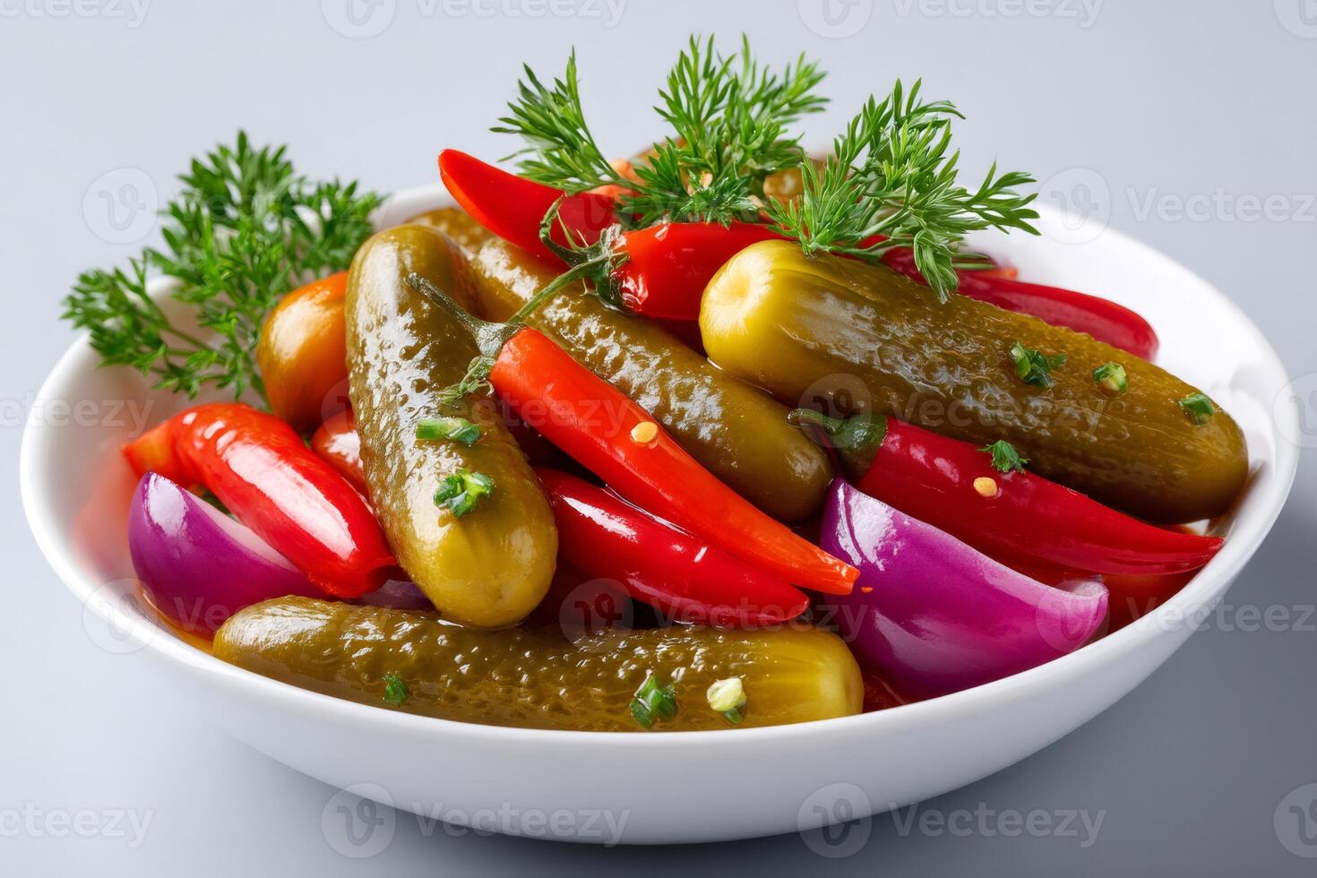 Pickled cucumbers, red chili peppers and red onions garnished with fresh dill are served in white bowl photo