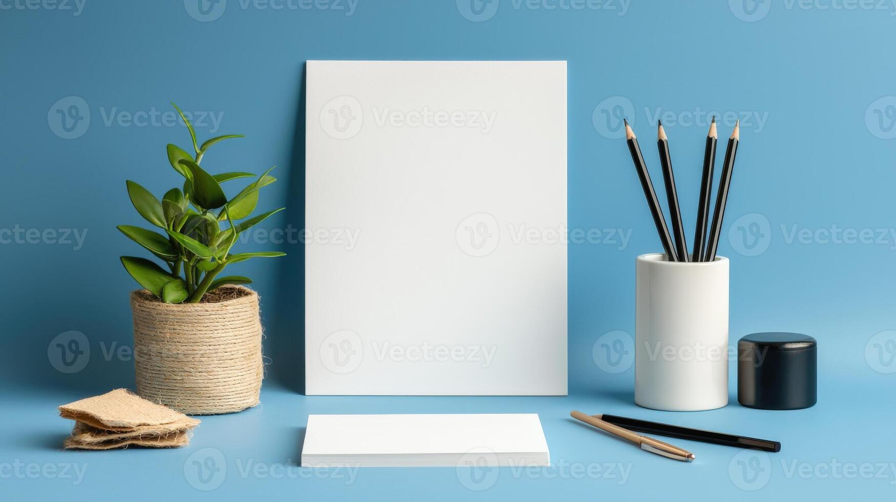 Blank white paper, pencils, and a plant on a blue background photo