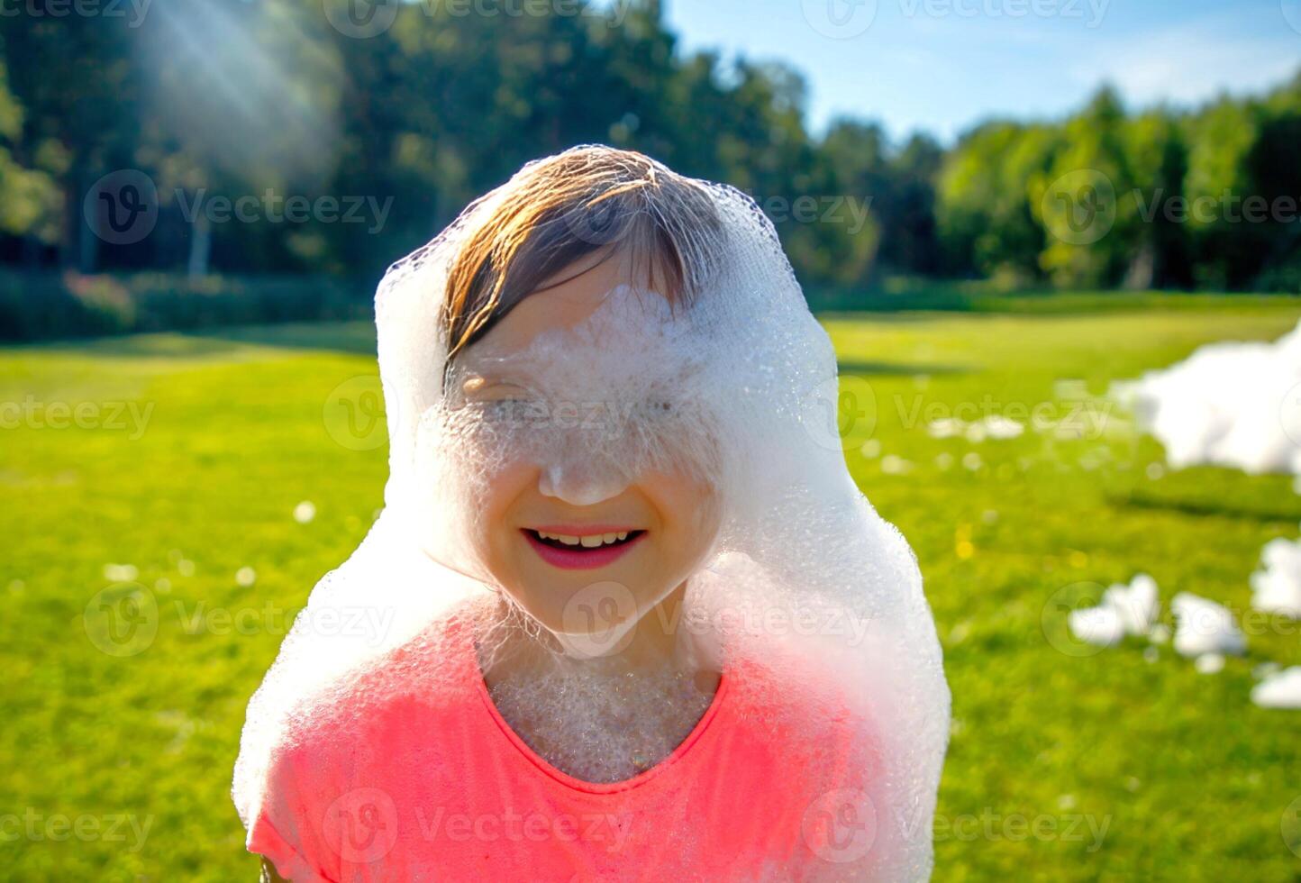 Toddler girl playing outdoors with soap bubbles on a sunny day.Girls face covered by bubbles foam. photo