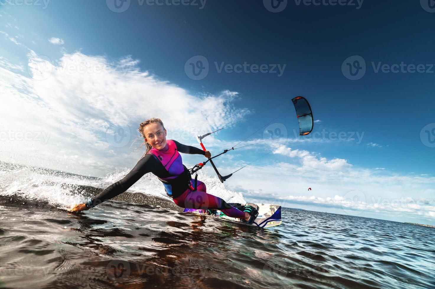 Kitesurfing girl in sexy wetsuit with kite in sky on board in blue sea riding on waves with water splash. Recreational activity, water sports, action, hobby and fun in summer. Kiteboarding sport photo