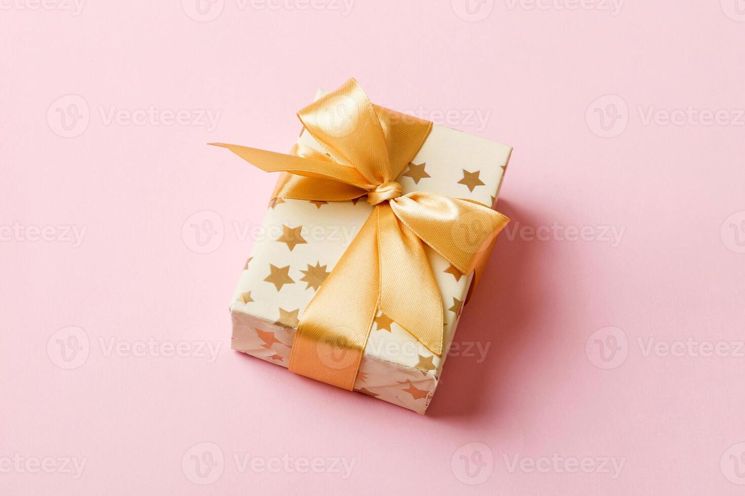 wrapped Christmas other holiday handmade present in white paper with gold ribbon on colored background. Present box, decoration of gift on colored table, top view photo