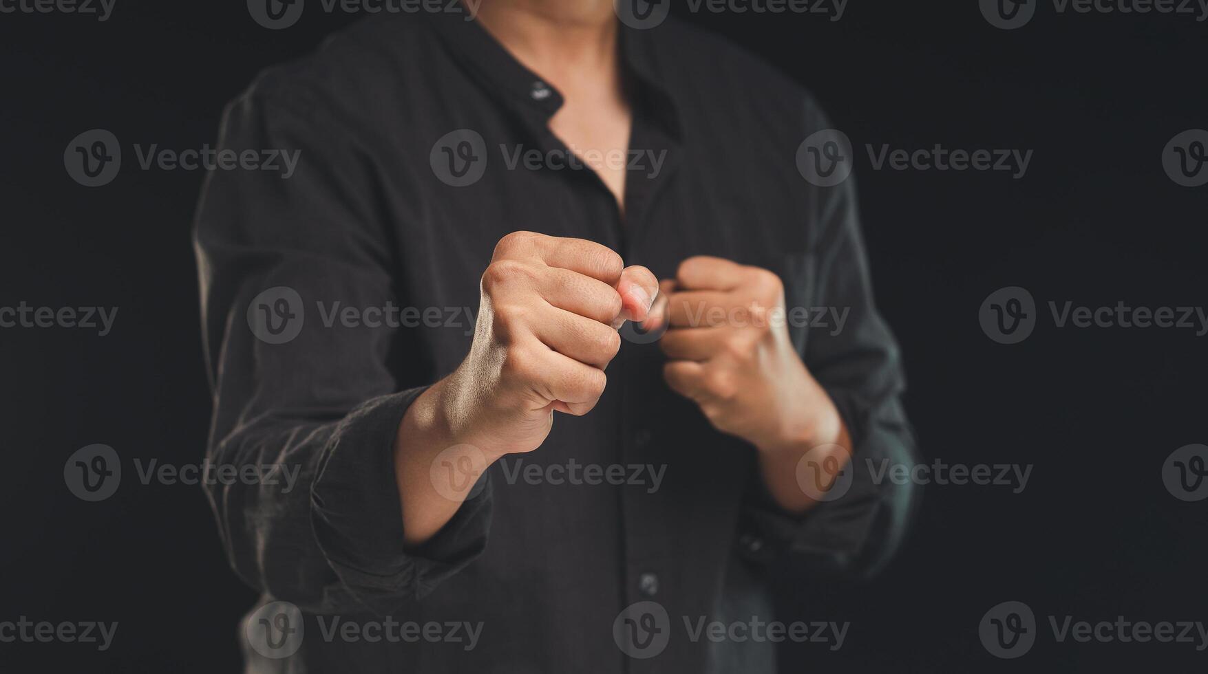A man in a black shirt raised his fists while standing against a black background photo