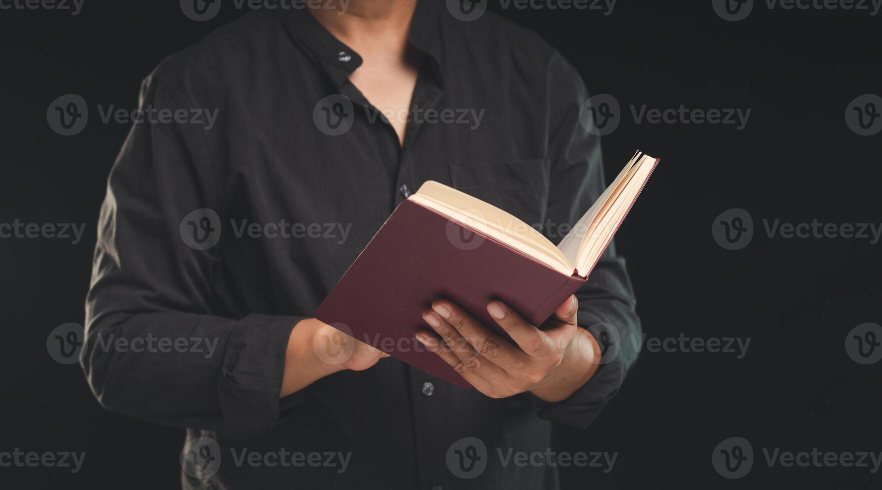 A man reading a book while standing against a black background photo