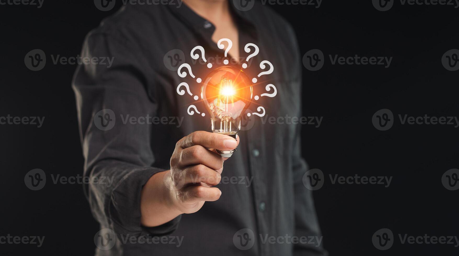 Hand holding a light bulb with question marks symbol while standing on a black background photo