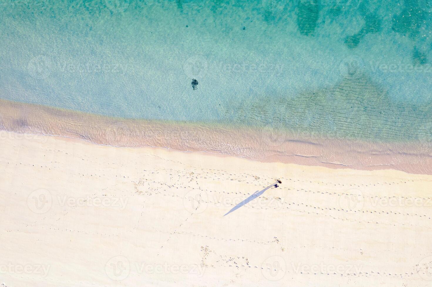 drone image of two person walking in beach shoreline with sand and water photo