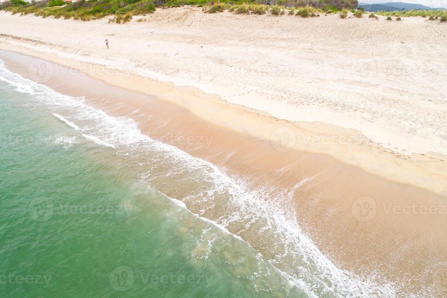 drone image of a person walking in beach shoreline with sand and water photo