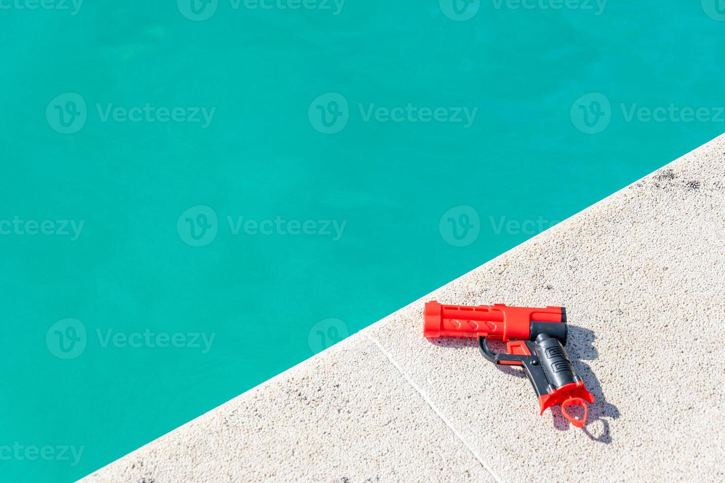 close view of a red and black toy gun near pool water, summer background concept photo