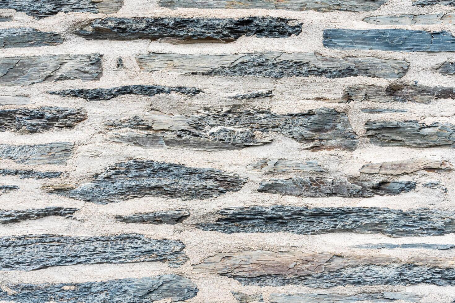 Close up of part of old stone wall with flat grey slate stones and mortar, textured and rustic background suitable for architectural and construction projects, photo