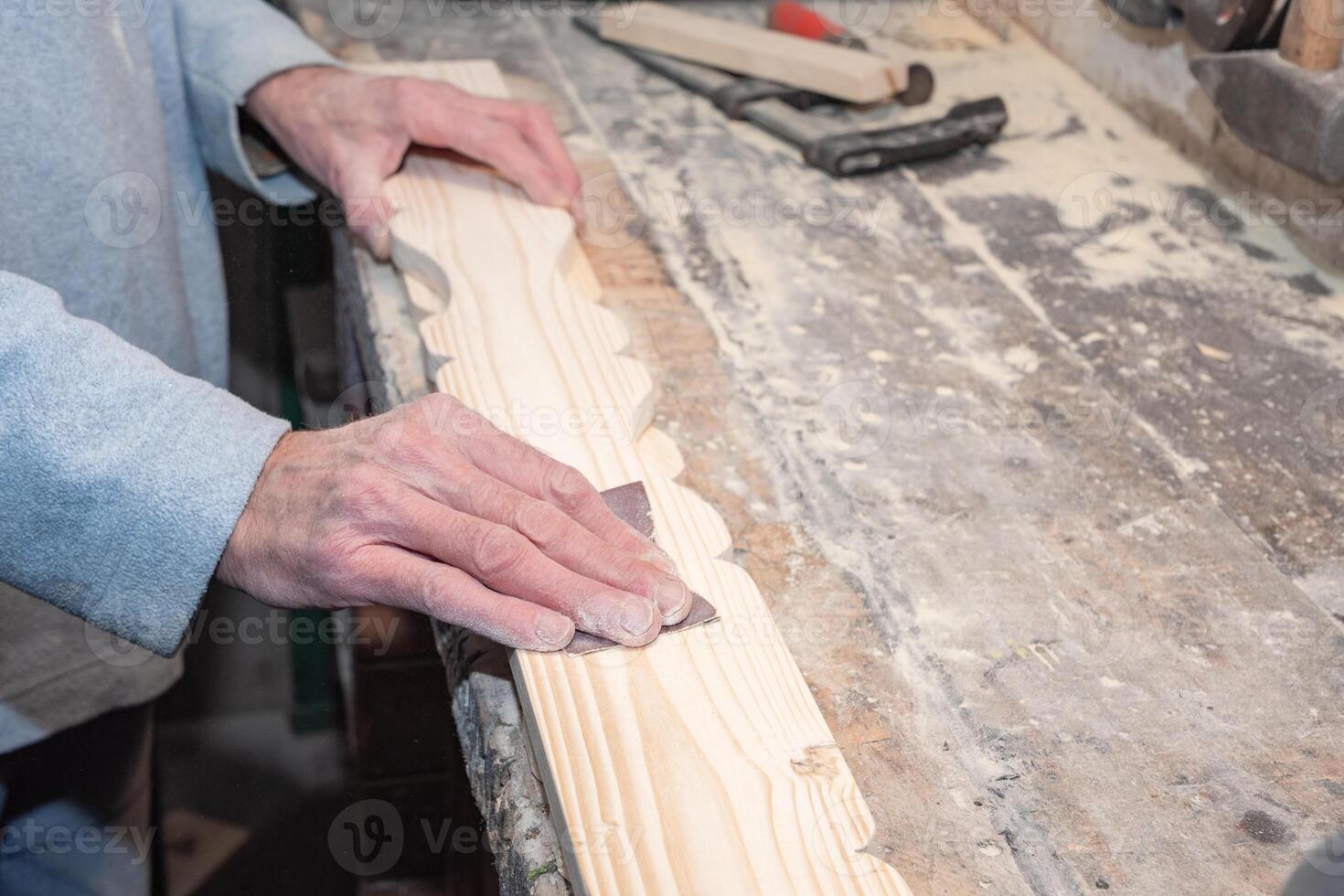 Close-up of carpenter's hands skillfully sanding decorative wooden plank on workbench in carpentry workshop, surrounded by various tools and small sawdust photo