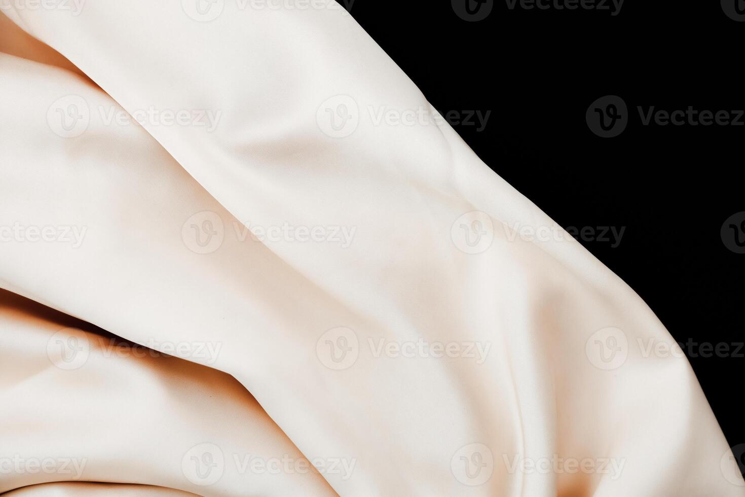Soft beige fabric draped elegantly on a dark background highlighting its texture and sheen photo
