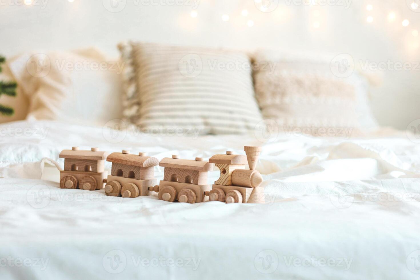 Wooden train set displayed on a cozy bed in a softly lit room with decorative pillows photo