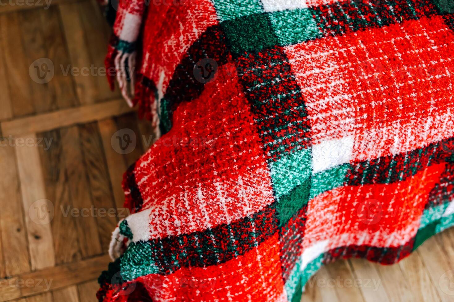 Cozy textured red and green blanket draped over wooden flooring during winter season photo
