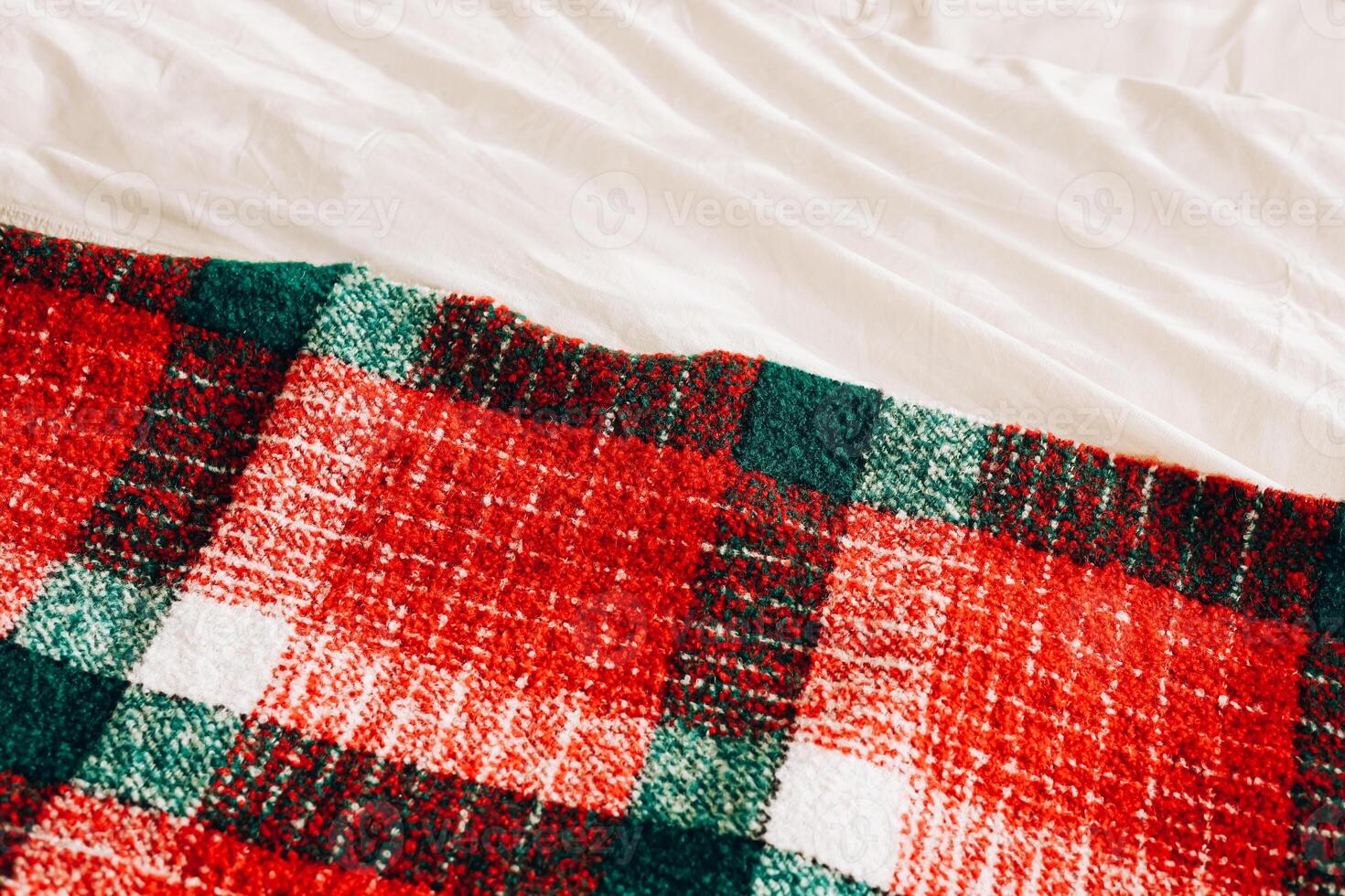 Cozy red and green plaid blanket draped over soft white bedding in a warm indoor setting photo