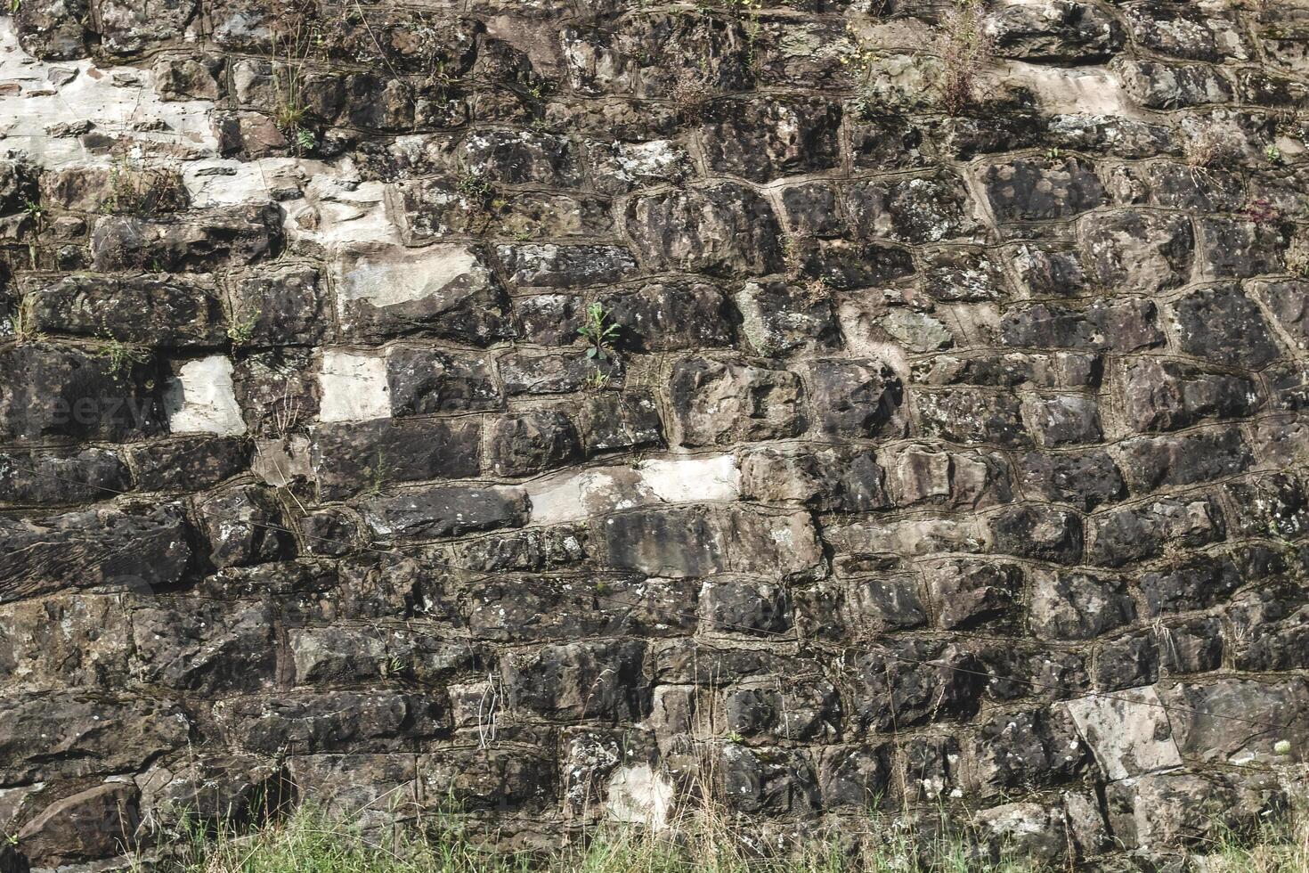 Detailed view of historic stone wall with moss and grass at the base in sunny daylight photo