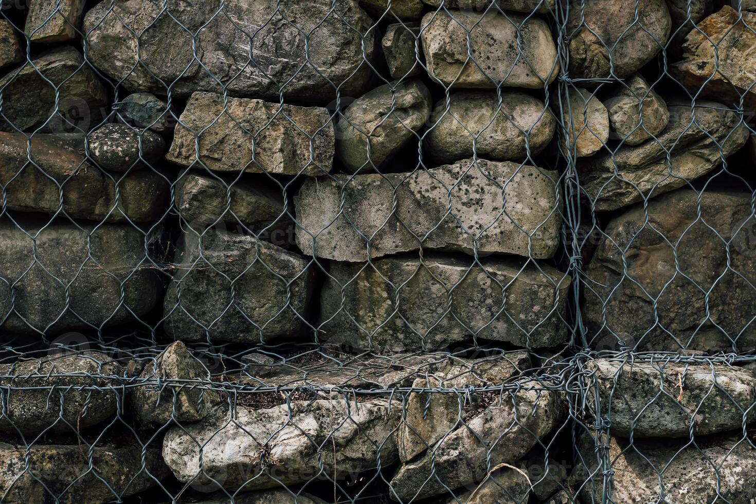 Rock wall construction method showcasing natural stones enclosed in wire mesh for stability photo