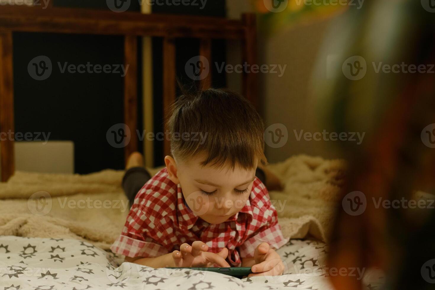 Kid is enjoying games on mobile phone, relaxing on bed at home photo