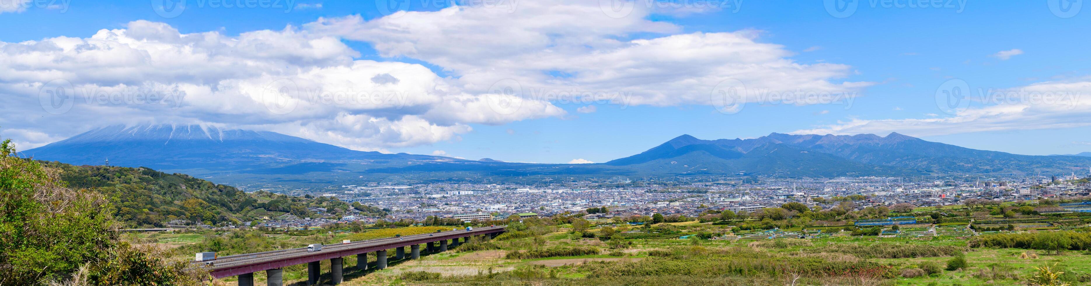 This panoramic landscape captures the peaceful coexistence of urban life and nature in rural Japan. In the distance, the iconic Mount Fuji rises majestically, photo