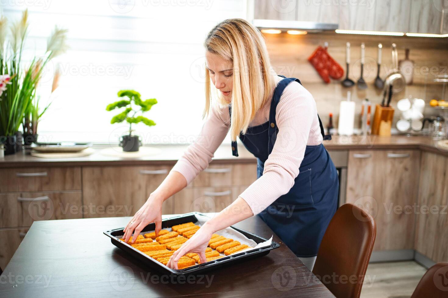 Home cook arranging freshly baked carrot sticks on a kitchen table photo