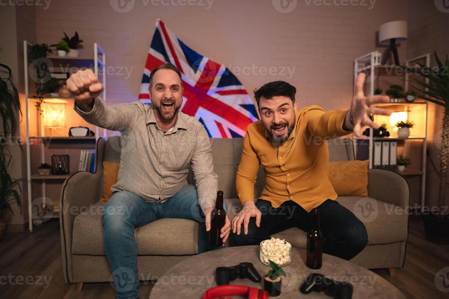 Friends celebrate victory while gaming in a cozy living room decorated with vibrant accents and a British flag photo