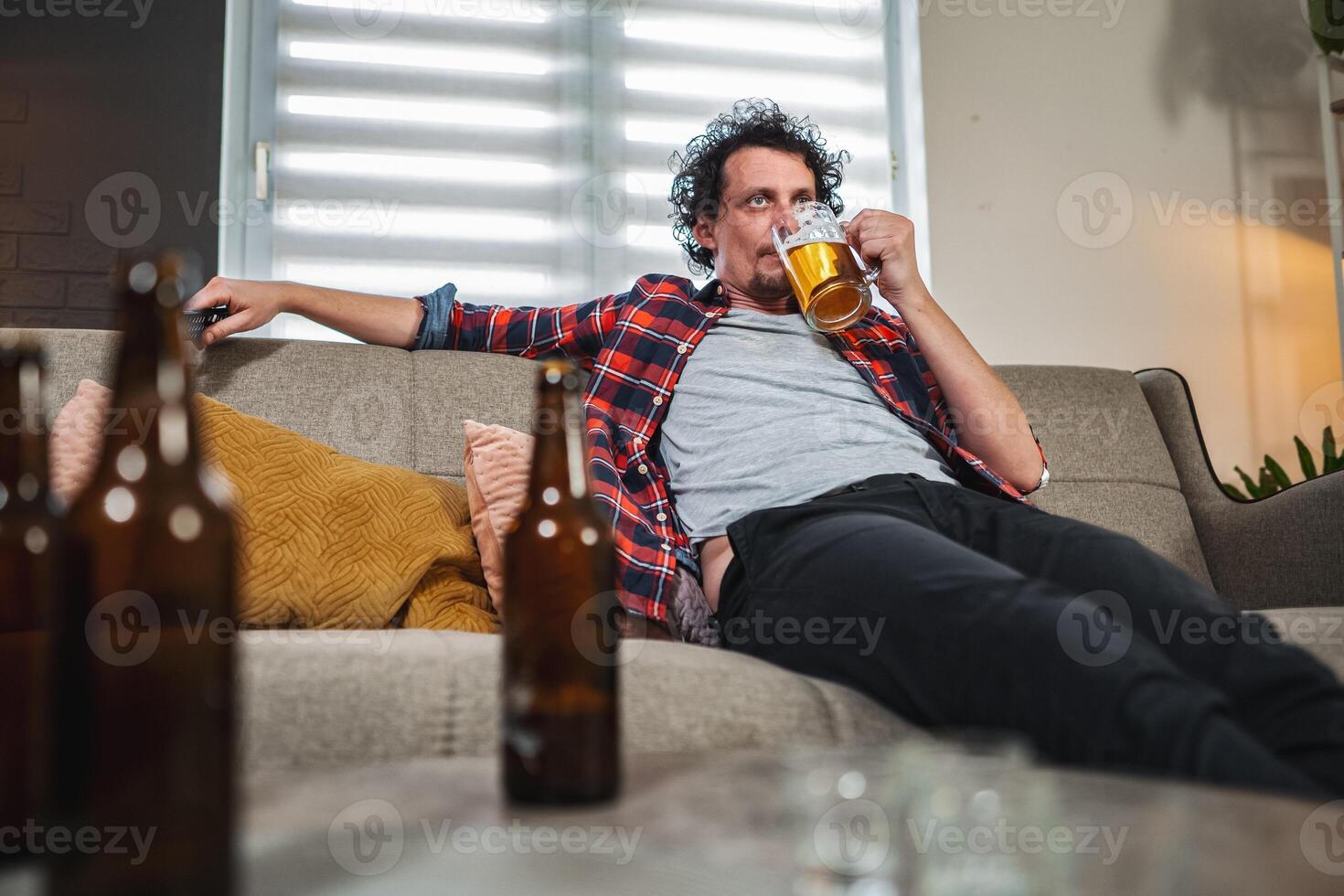 Mid adult man drinking beer at home on sofa photo