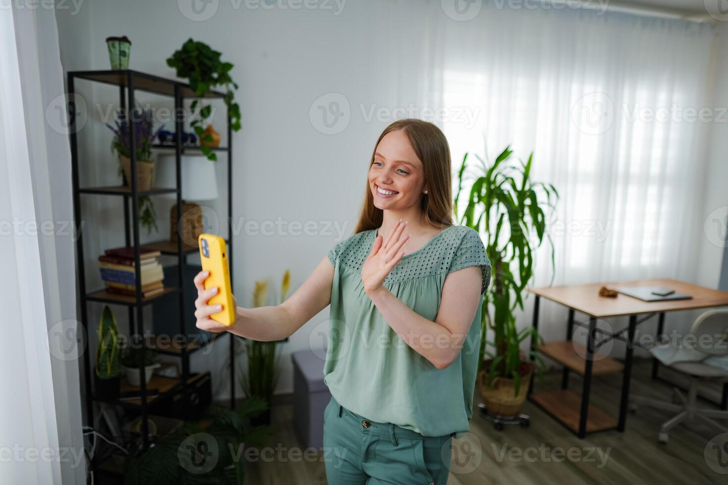 Smiling woman waving at friends during a virtual call at home photo