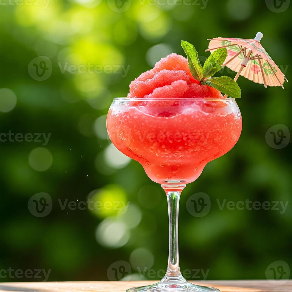 A vibrant red frozen cocktail in a glass garnished with mint and a small umbrella, set against a green bokeh background photo
