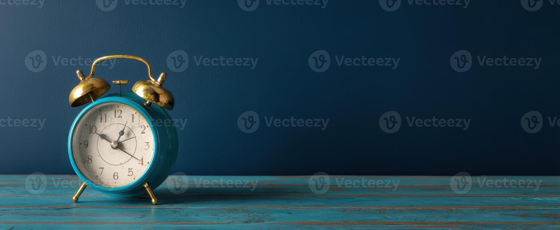 The vibrant blue alarm clock on wooden table against a dark background. photo
