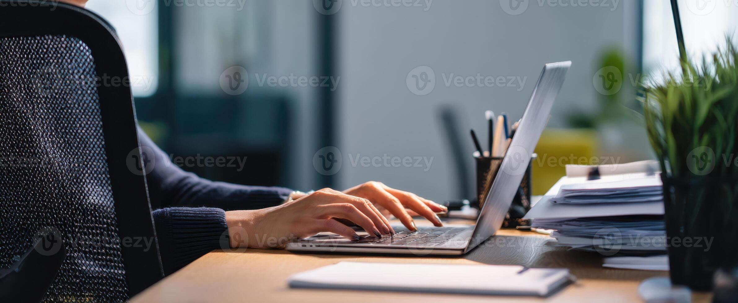 The hands typing on a laptop in a modern workspace with plant and documents. photo