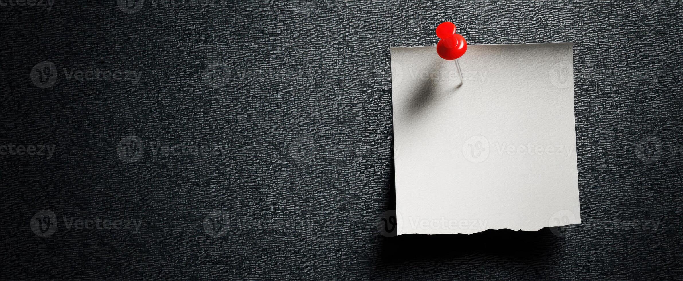 The simple red pushpin holding a blank note on a textured black background. photo