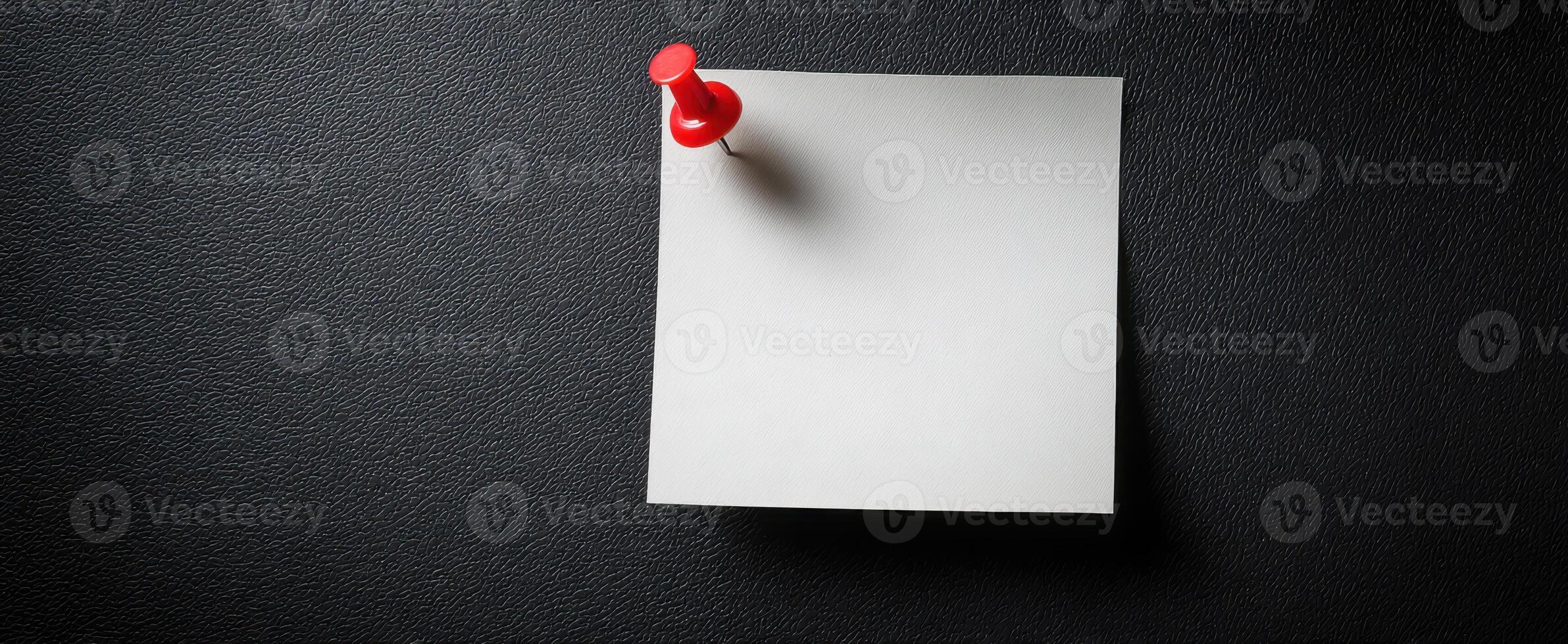 The red pushpin holding a blank note on a textured black surface. photo
