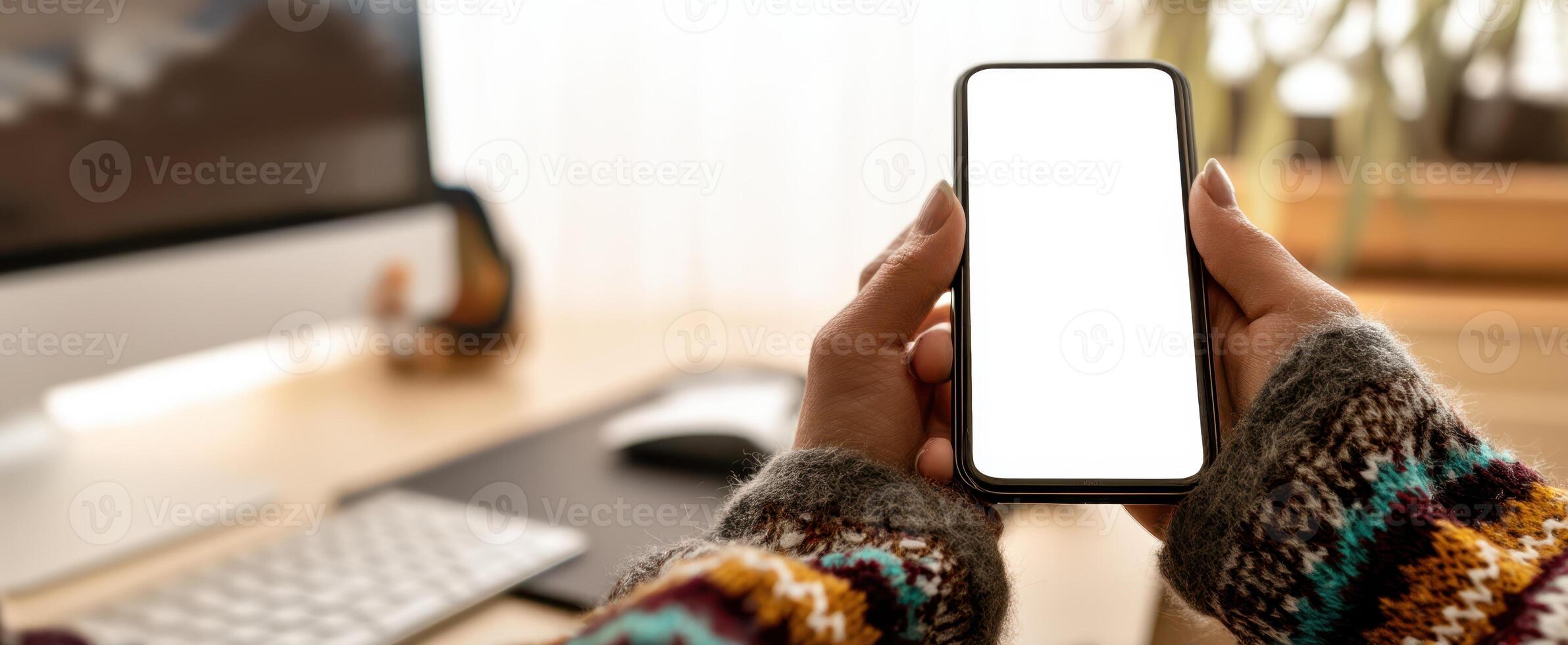 The smartphone held in hands showcasing a blank screen in a cozy workspace. photo