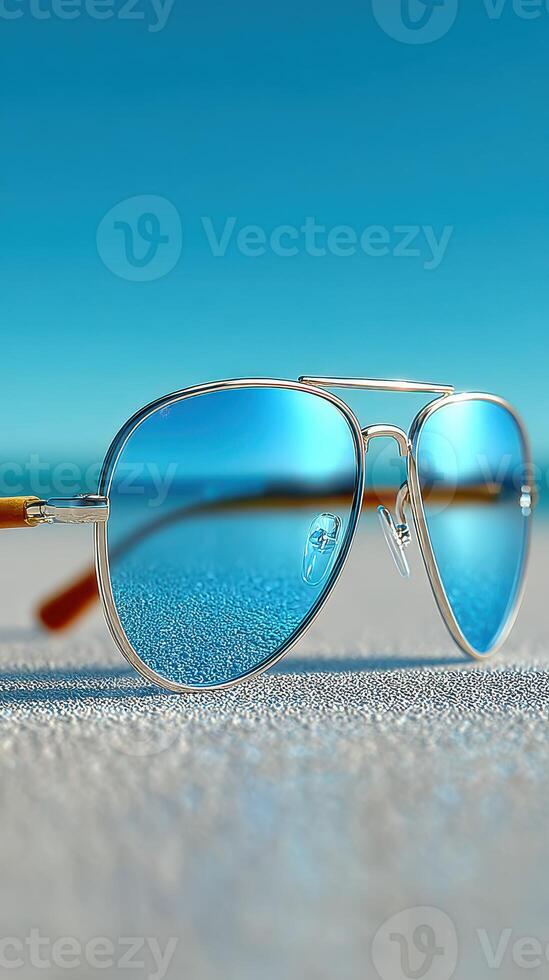 Stylish sunglasses resting on a sandy beach with clear blue skies and the ocean in the background during midday photo