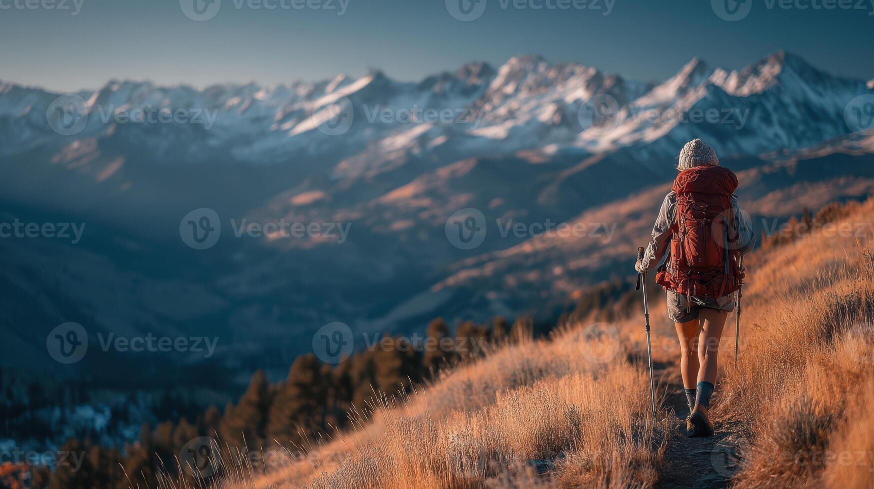 Hiker explores a mountain trail at dusk surrounded by snow-capped peaks and golden grass near a scenic wilderness photo