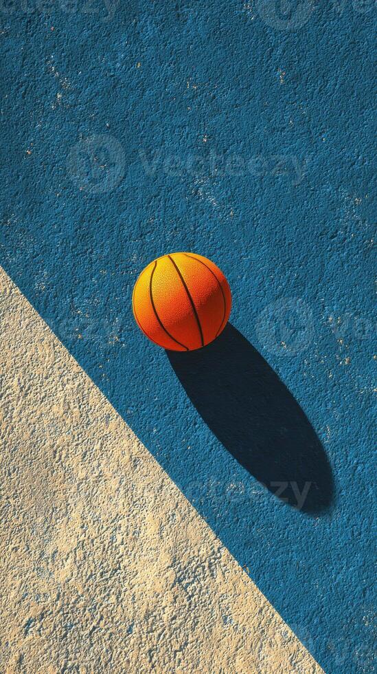 Bright orange basketball resting on the blue and white textured court during sunny daylight hours photo