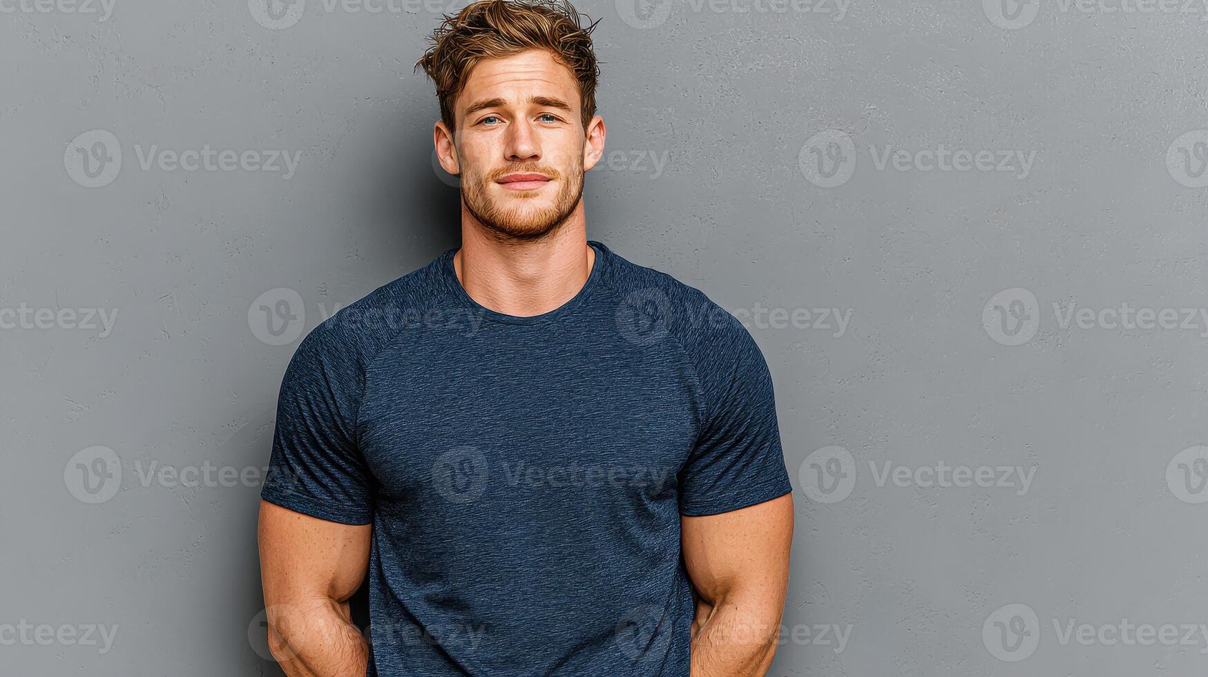 Young man in casual attire poses confidently against a gray wall, showcasing a relaxed yet stylish demeanor in a modern setting photo